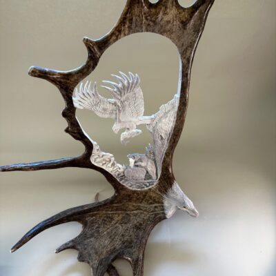 Unique Antler designs a hand carved moose antler carving depicts an eagle soaring, with its catch, high above a fishing bear.  This carving is based with a strong sturdy antler. All of our Last Catch designs come with an eagle head with a shined beak at the rosette.